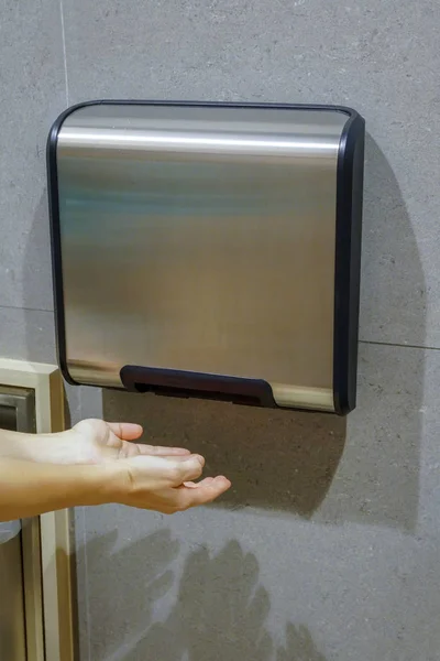 Woman hands dries wet hand in modern vertical hand dryer in publ