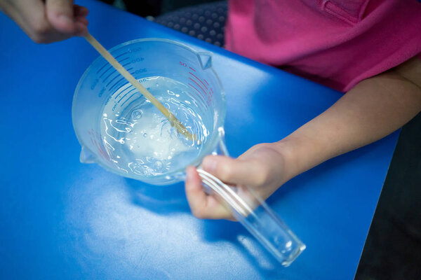 Kid hand stirring white powder in measuring cup with wood chopst