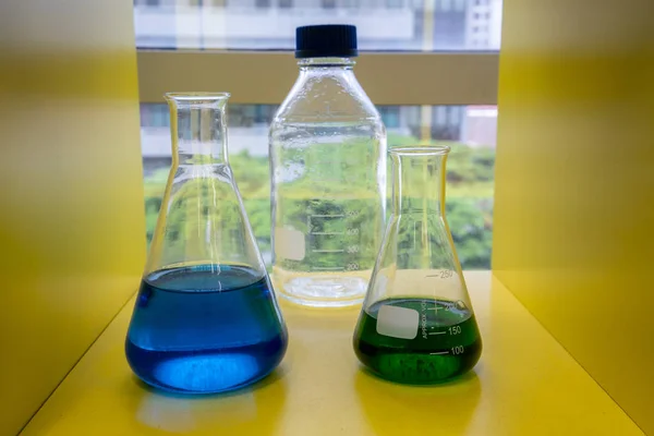 Solução azul e verde nos copos de vidro na prateleira amarela — Fotografia de Stock