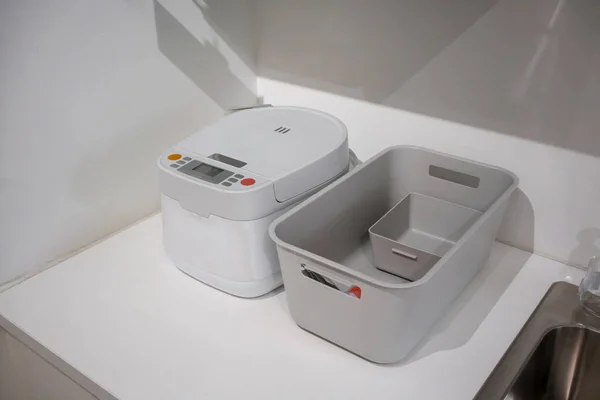 Біла електрична рисова плита і сірий пластиковий кошик на кухні si — стокове фото