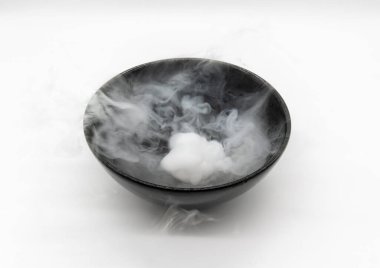 Temiz Duman ve Buhar, beyaz arka planda izole edilmiş siyah bir kase kuru buzun üzerinde hareket halinde. Yüzeyde kaynayan karbondioksit gazı.
