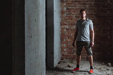 Bir onay gömlek ve şort bir tuğla duvara giyen genç adam.