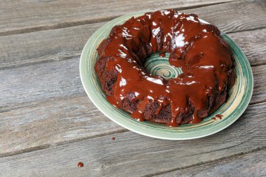 Kek çikolata ahşap masa üzerinde yeşil bir tabakta ile drizzled.