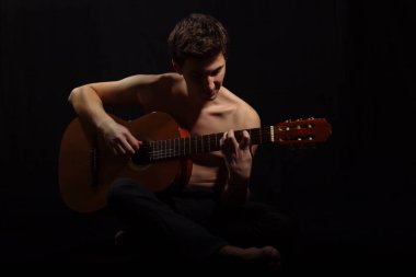 Üstsüz kaslı adam gitar çalıyor. Siyah arka plan.