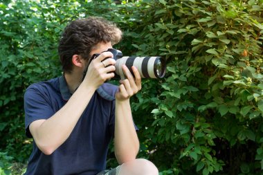 Fotoğraf götüren bir portre fotoğrafçısı. Yeşil çalılar arka planda.