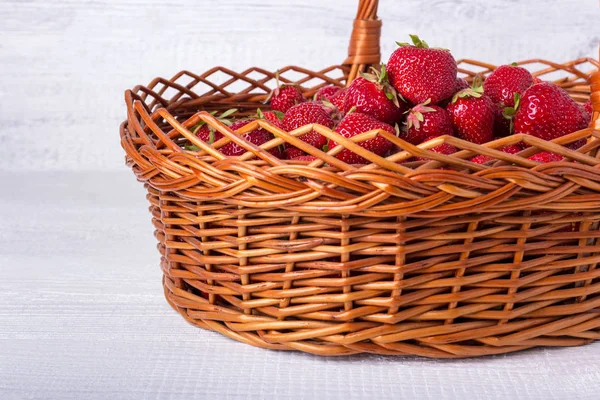 Wiklinowy koszyk pełen dojrzałych truskawek. Na białym tle drewnianych. — Zdjęcie stockowe