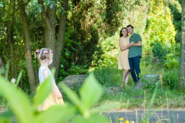 Ön planda arka kız duruyor. Birbirimizi ona baktığını kucaklayan arka plan ebeveynler.