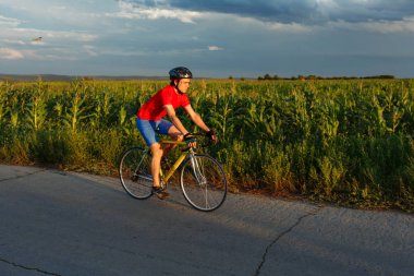 Bir bisikletçi alan boyunca yol bisiklet sürmek. Güzel bir mavi gökyüzü arka planda.