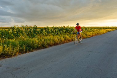 Bir bisikletçi alan boyunca yol bisiklet sürmek. Arka plan günbatımı gökyüzünde.