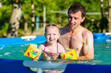 Baba ve kızı Havuzda yüzmek. Kız yastıklar yüzüyor.
