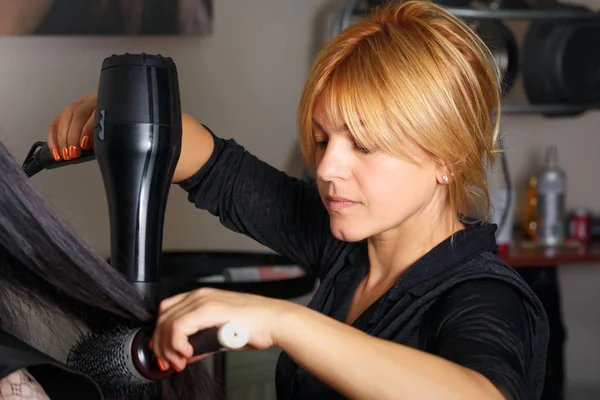 Estilista de cabelo profissional com secador de cabelo e pente trabalhando no cabelo do cliente . — Fotografia de Stock