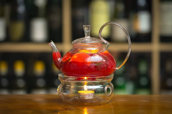 Красный чай в чайнике на стойке со свечой на деревянной барной стойке. На заднем плане стойка с бутылками . — стоковое фото