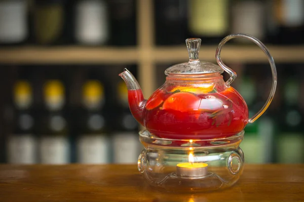 Ahşap bar counter üzerine de mum ile bir stand bir çaydanlık kırmızı çay. Arka plan rafa şişe ile.