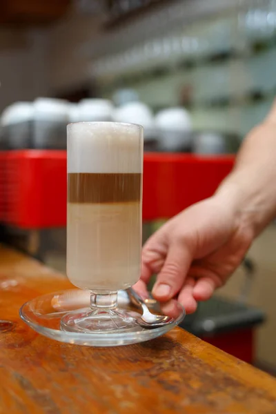 Ręka trzyma barista i serwujemy szklankę latte. — Zdjęcie stockowe