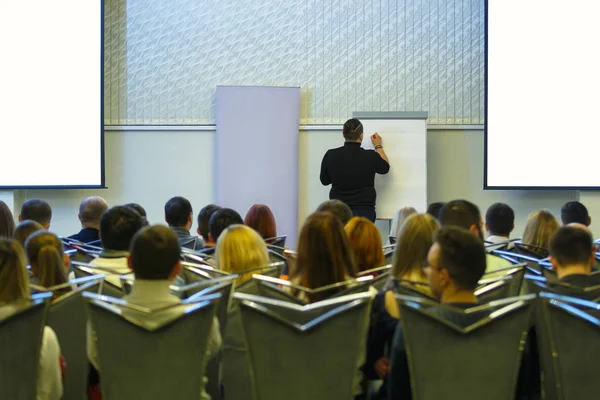 Speaker back to audience is going to write on board. Business meeting. Audience in the conference hall. Screens on the sides are isolated.