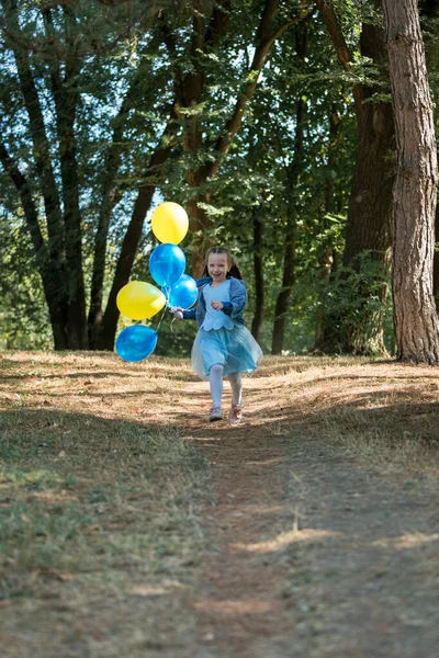 En söt liten flicka som springer i parken med en massa ballonger. Hon skrattar provocerande. Begreppet lycklig barndom. — Stockfoto