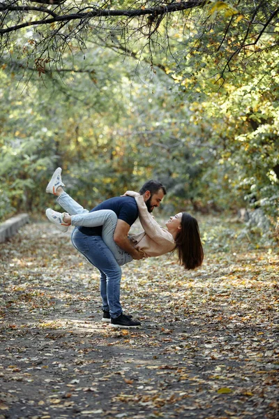 Junges schönes Paar im Park. Ein Mann hält eine Frau auf dem Arm. im Hintergrund Herbstwald. — Stockfoto