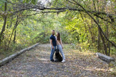 Genç ve güzel bir çift ve labradorları parkta yürüyorlar. Erkek, kadın ve köpek. Ormanda ılık bir sonbahar akşamı.