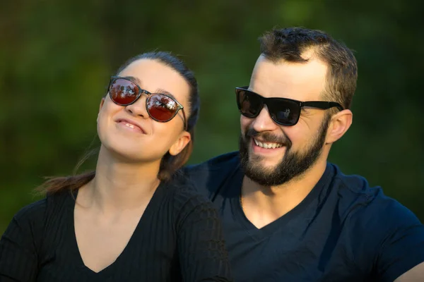 Ormanda güneş gözlüğü takmış bir adam ve bir kadının portresi. Doğanın arka planında genç ve şık bir çift. Ormanda ılık bir sonbahar akşamı. — Stok fotoğraf