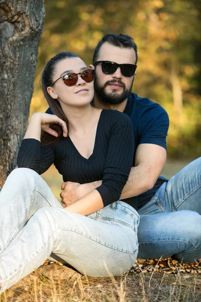 Retrato de un hombre y una mujer en gafas de sol en el bosque. Joven pareja elegante en el fondo de la naturaleza. Cálida tarde de otoño en el bosque . — Foto de Stock