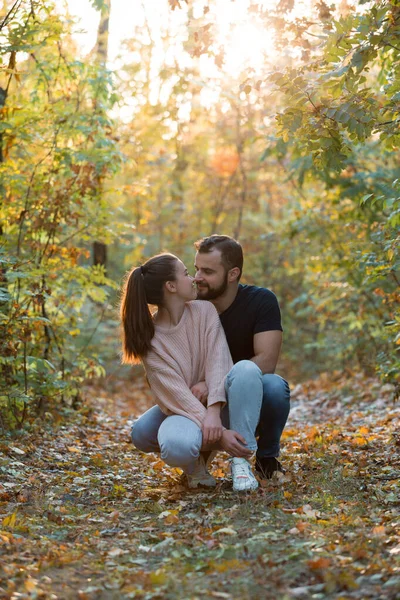 Pareja joven enamorada abrazándose en el Parque. Hombre y mujer a solas. Cálida noche de otoño en el bosque. Rayos del sol poniente rompen las ramas de los árboles . — Foto de Stock