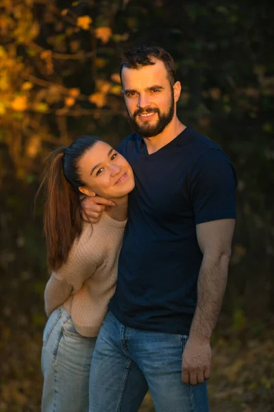 Junges schönes Paar im Park. Sie werden von einem Sonnenstrahl beleuchtet. im Hintergrund Herbstwald. — Stockfoto