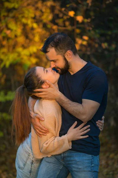 Casal jovem apaixonado abraçando e beijando no Parque. Eles são iluminados por um raio de luz solar. No fundo floresta de outono . — Fotografia de Stock