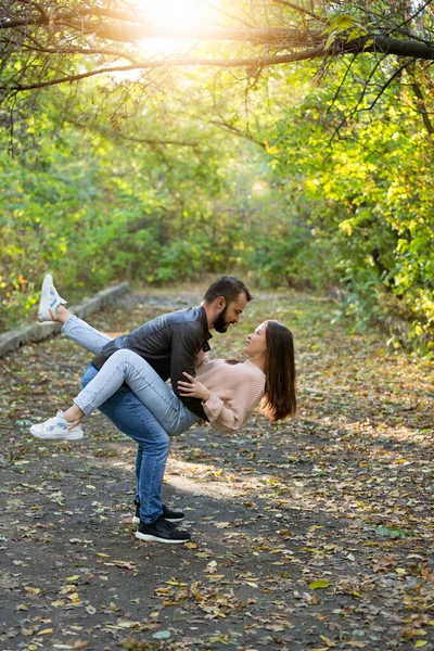 Fiatal, gyönyörű pár a parkban. Egy férfi egy nőt tart a karjaiban. A háttérben őszi erdő. — Stock Fotó