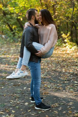 Parktaki genç ve güzel çift. Bir adam bir kadını kollarında tutuyor. Arka planda sonbahar ormanında.
