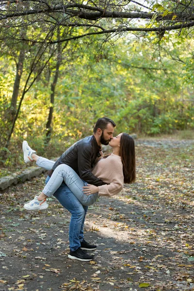 Młoda piękna para w parku. Mężczyzna trzyma kobietę w ramionach. W tle jesienny las. — Zdjęcie stockowe