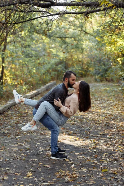 Fiatal, gyönyörű pár a parkban. Egy férfi egy nőt tart a karjaiban. A háttérben őszi erdő. — Stock Fotó