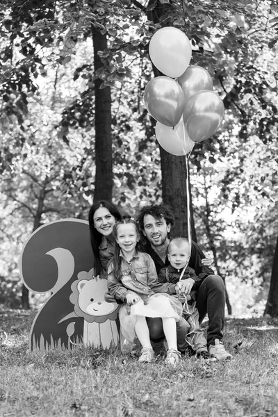 Familjeliv. Porträtt av föräldrar och deras barn i parken. Födelsedag för en tvåårig pojke. Dekor med nummer två med lejon och ballonger. — Stockfoto