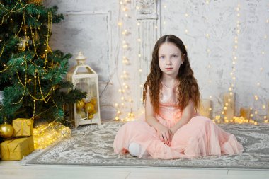 Noel ağacında oturan küçük tatlı kız. Evde yeni yıl odası var. Noel neşesi. Yaşam tarzı, aile ve tatil.