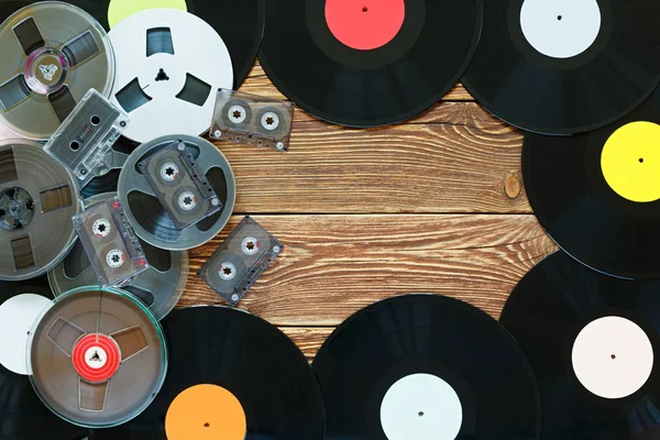 Viejas bobinas vintage, discos de vinilo y cintas de cassette sobre un fondo de mesa de madera. Etiquetas multicolores. Vista superior. Lugar para copiar espacio . — Foto de Stock