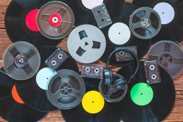 Antiguas bobinas vintage, discos de vinilo, cintas de cassette y auriculares sobre un fondo de mesa de madera. Etiquetas multicolores. Vista superior . — Foto de Stock