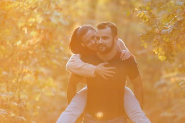 Genç ve güzel bir çift ve parktaki labradorları. Bir adam bir kadını sırtında tutuyor ve kadın ona sarılıyor. Ormanda ılık bir sonbahar akşamı.