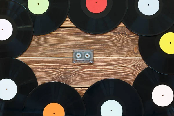 Una cinta de cassette vintage y discos de vinilo sobre un fondo de mesa de madera. Etiquetas multicolores. Vista superior. Lugar para copiar espacio . — Foto de Stock