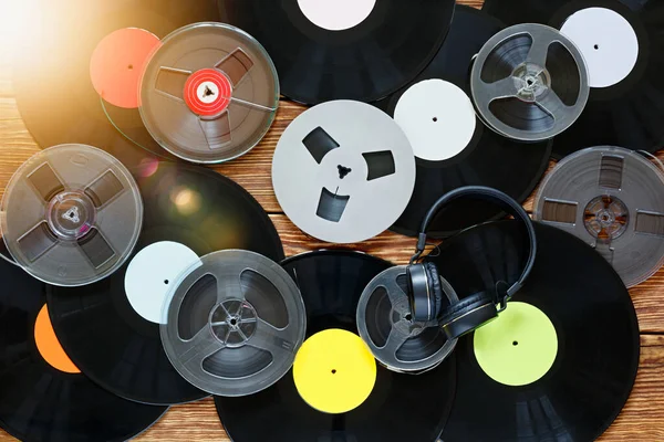 Antiguas bobinas vintage, discos de vinilo, cintas de cassette y auriculares sobre un fondo de mesa de madera. Etiquetas multicolores. Vista superior. Deslumbramiento solar . — Foto de Stock