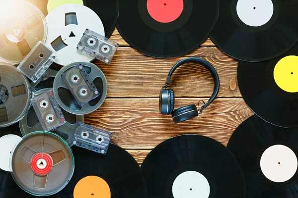 Anciennes bobines vintage, disques vinyles, cassettes et écouteurs sur un fond de table en bois. Étiquettes multicolores. Vue de dessus. Éblouissement du soleil . Photos De Stock Libres De Droits