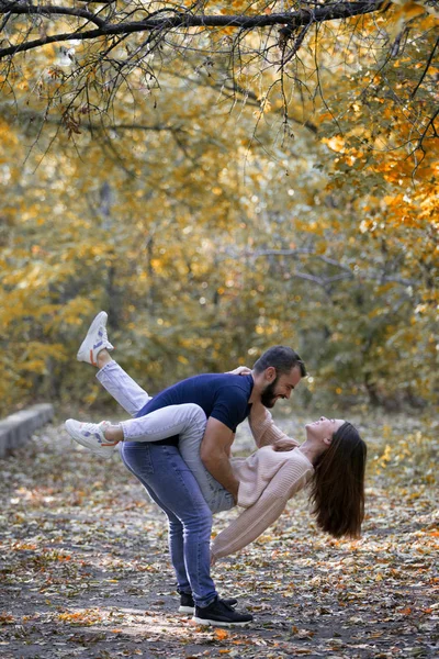 Junges schönes Paar im Park. Ein Mann hält eine Frau auf dem Arm. im Hintergrund Herbstwald. — Stockfoto