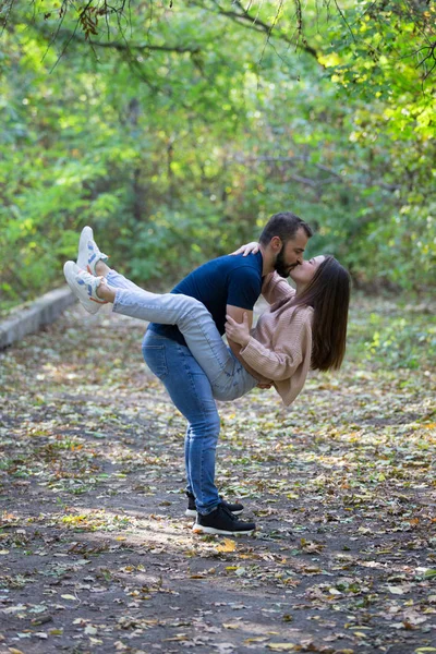 Hermosa pareja joven en el Parque. Un hombre sostiene a una mujer en sus brazos. En el bosque de otoño de fondo . — Foto de Stock