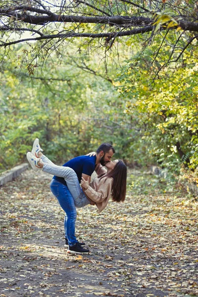 Hermosa pareja joven en el Parque. Un hombre sostiene a una mujer en sus brazos. En el bosque de otoño de fondo . — Foto de Stock