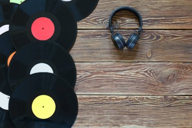 Ahşap masa arka planında Retro plaklar ve kulaklıklar. Çok renkli etiketler var. Üst Manzara. Boşluğun kopyalanacağı yer.