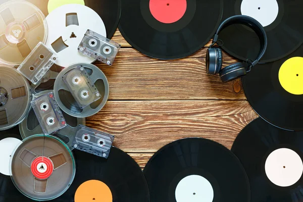 Antiguas bobinas vintage, discos de vinilo, cintas de cassette y auriculares sobre un fondo de mesa de madera. Etiquetas multicolores. Vista superior. Lugar para copiar espacio. Deslumbramiento solar . — Foto de Stock