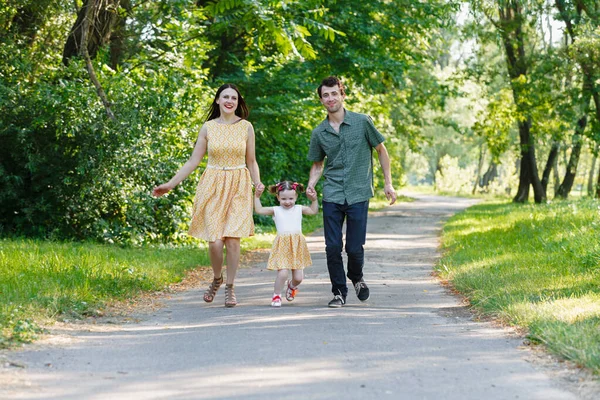 Щаслива сім'я бігає по шляху тримаючись за руки і проводячи час у прекрасному зеленому парку. Жінка вагітна . — стокове фото