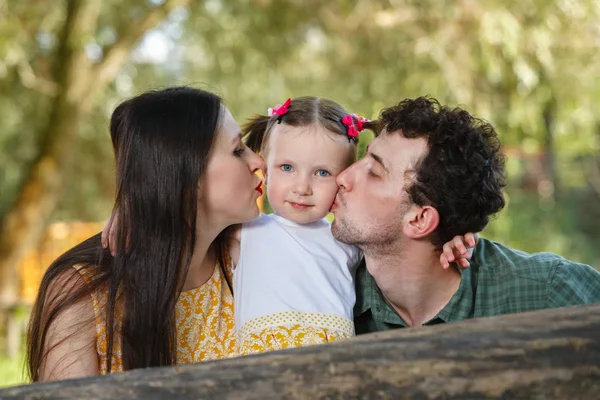 Ebeveynlerin ve kızların aile portresi. Bir erkek ve bir kadın kızı yanaklarından öperler. Arkaplanda doğa. — Stok fotoğraf