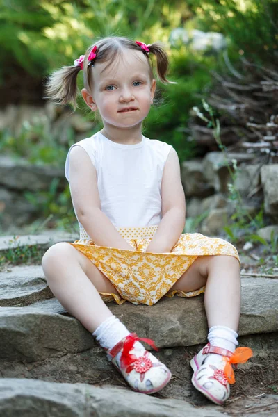 Retrato de una linda niña en el fondo de la naturaleza. Está sentada en las rocas. . — Foto de Stock