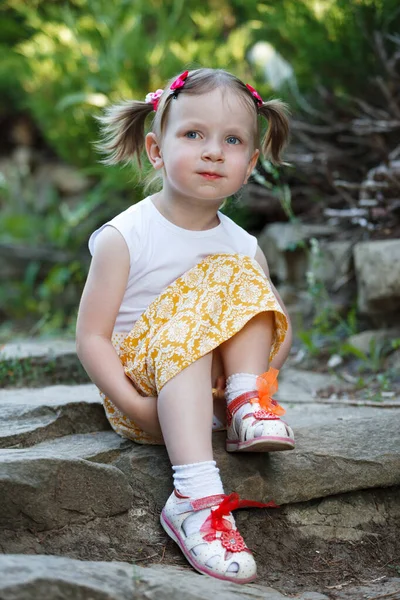 Retrato de una linda niña en el fondo de la naturaleza. Está sentada en las rocas. . — Foto de Stock