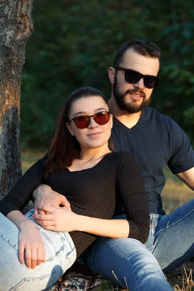 Retrato de un hombre y una mujer en gafas de sol en el bosque. Joven pareja elegante en el fondo de la naturaleza. Cálida tarde de otoño en el bosque . — Foto de Stock