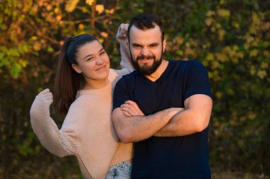 Parktaki genç ve güzel çift. Oynaşıp eğleniyorlar. Kız gücünü gösteriyor. Bir güneş ışınıyla aydınlatılıyorlardı. Arka planda sonbahar ormanında.